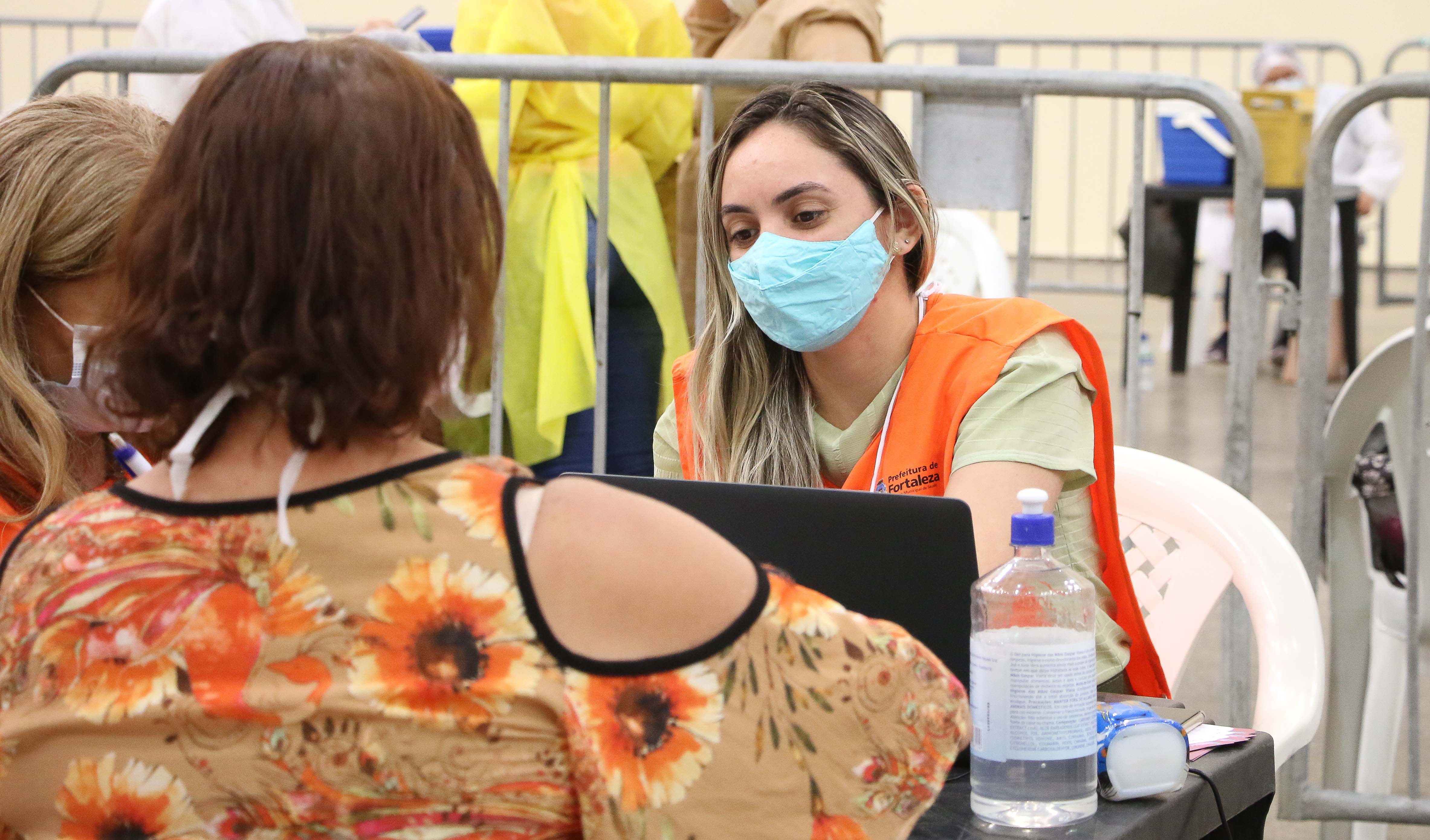 enfermeira de másca sentada em atendimento, de frente para mulher de costas